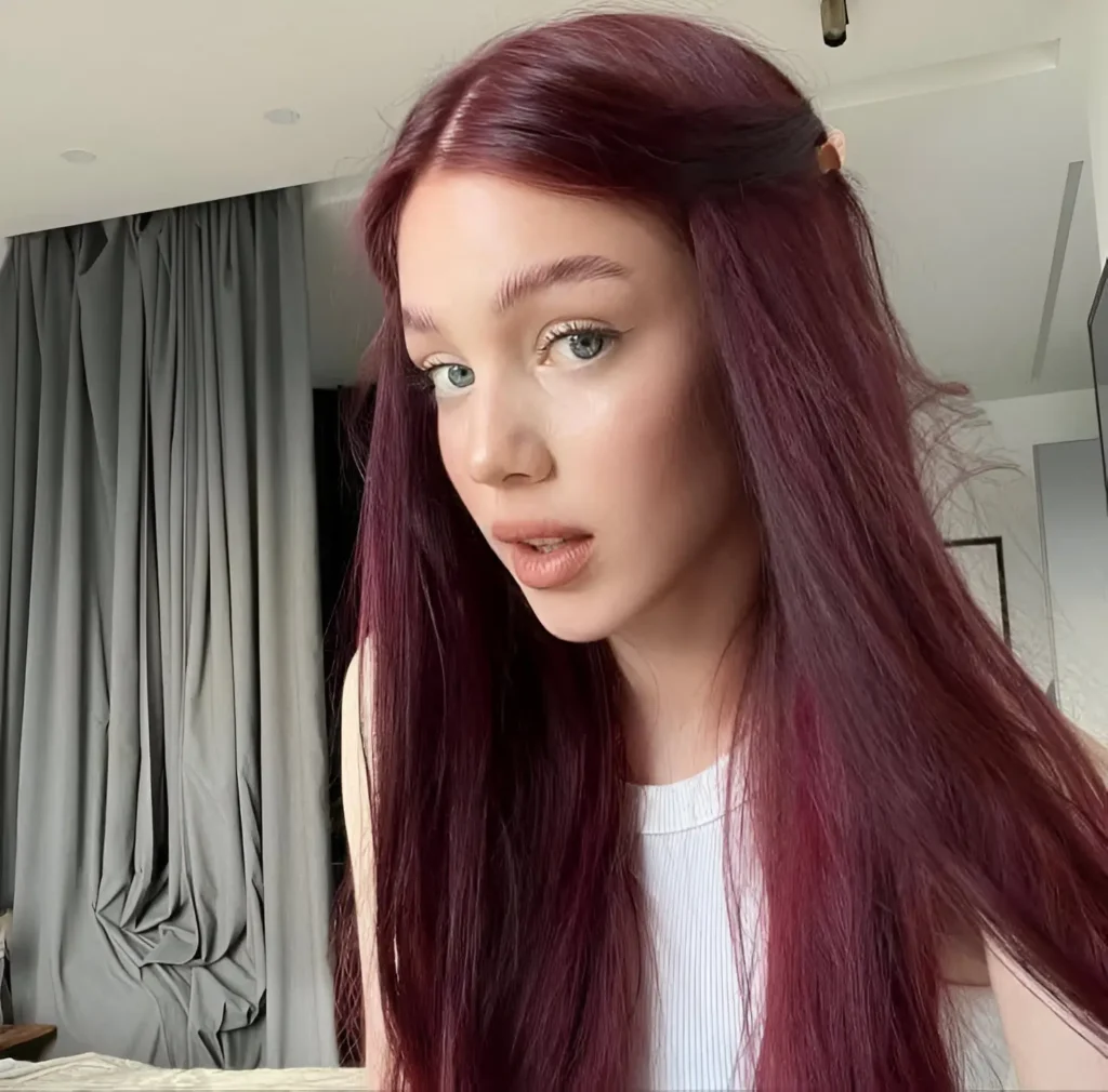 Woman with long, slightly wavy, muted burgundy hair with visible plum undertones.