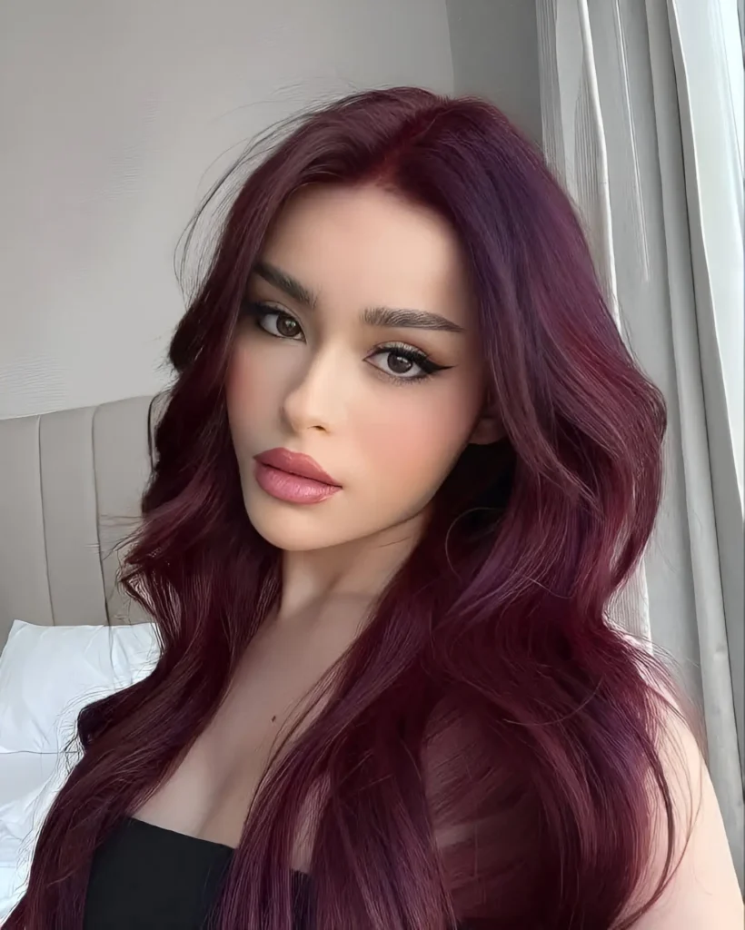 Woman with long, wavy burgundy hair with prominent violet undertones.