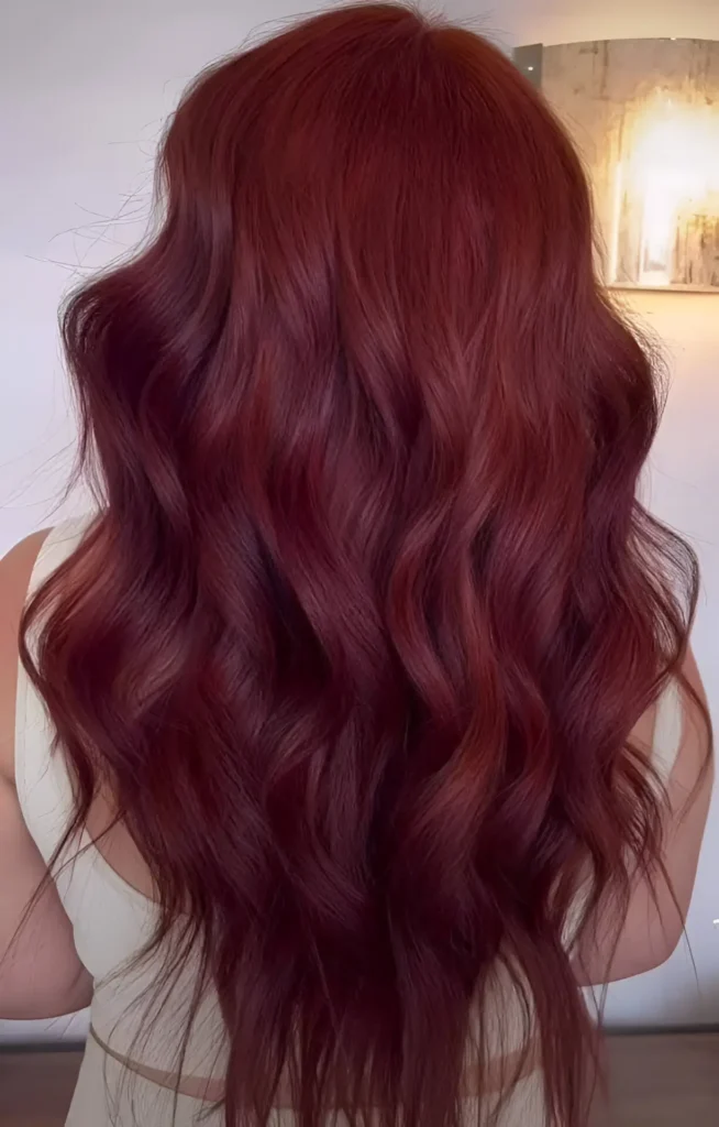 Person with long, wavy, auburn-infused burgundy hair, viewed from the back.