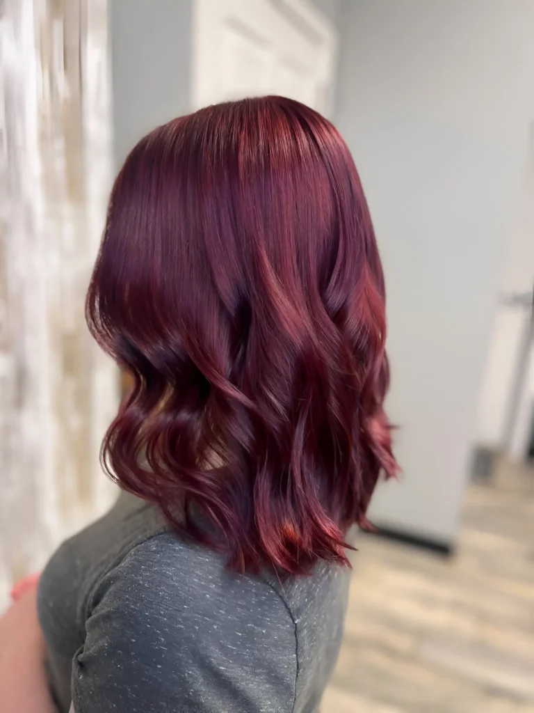 Woman with shoulder-length, wavy burgundy hair with subtle copper highlights.