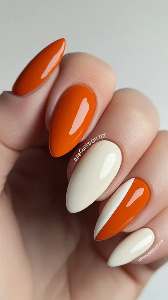 Hand showing rounded nails with a modern geometric color block design using glossy burnt orange and cream polish.