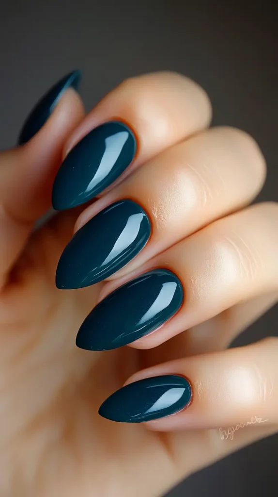 Hand showing elegant rounded nails painted in a glossy, deep teal or dark turquoise crème polish.