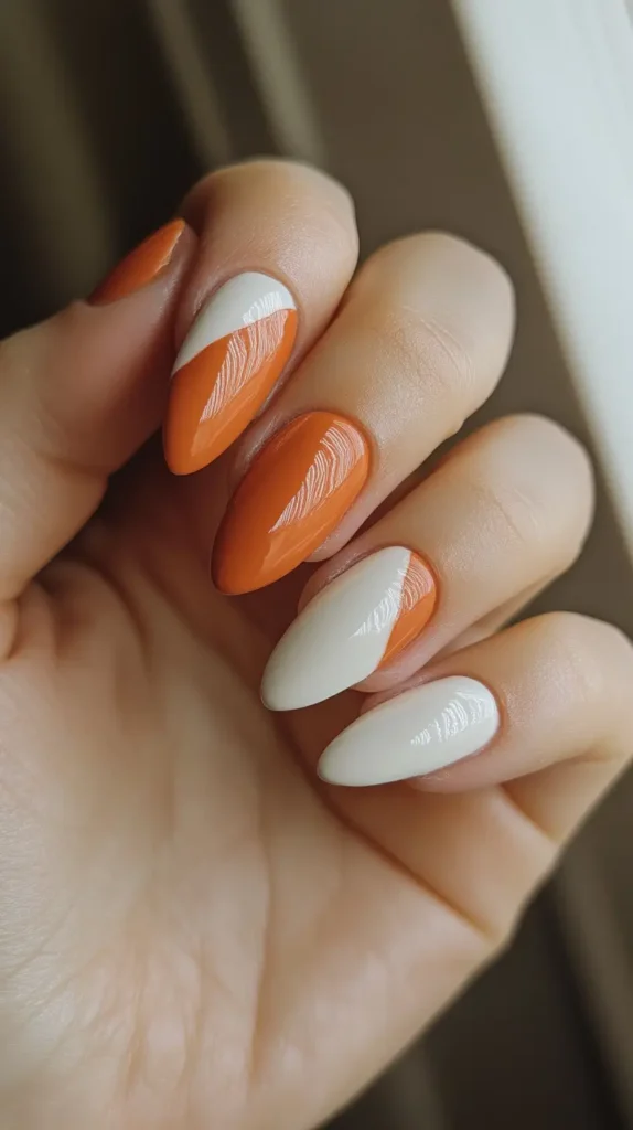 Close-up of almond-shaped nails featuring a diagonal color block design with glossy terracotta orange and creamy off-white polish creating a sharp line.