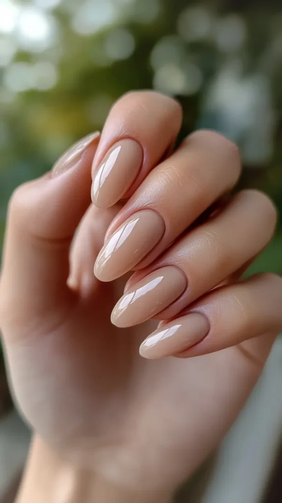 Close-up of short round nails painted with a glossy, bright classic red polish, hand holding a small green leaf.