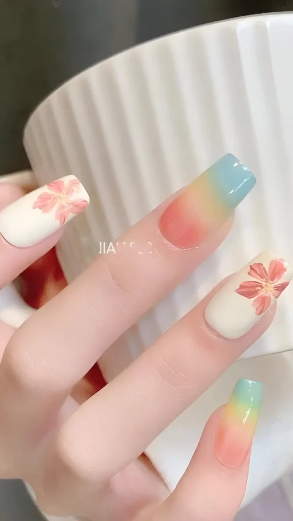 Cute nail design combining vertical sunrise ombre (blue, yellow, coral) and delicate pink floral art on creamy base nails; medium square shape.