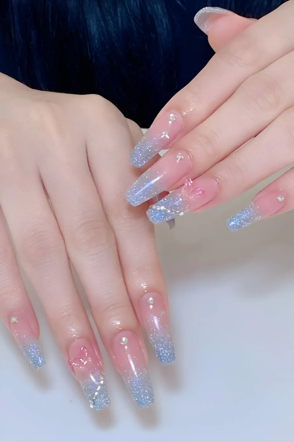 Cute long coffin nails with sheer pink base, icy blue glitter ombre tips, and small rhinestone details near cuticles.