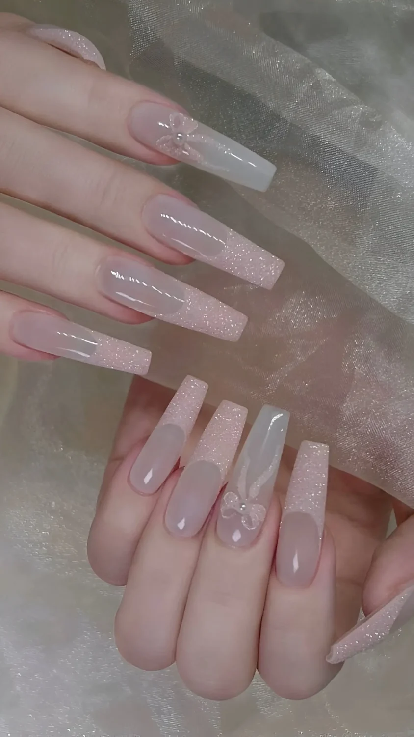 Cute long square nude nails with subtle glitter and translucent 3D bow accents.