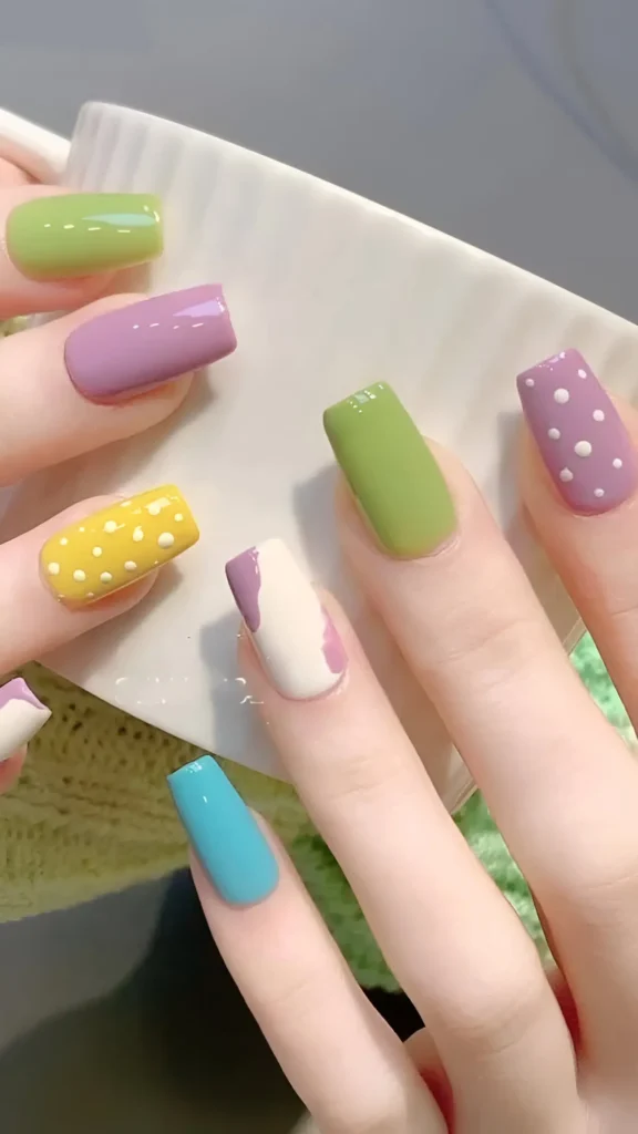 Cute nail design featuring mix-and-match pastel and bright colors (lime, lavender, yellow, turquoise) with patterns including polka dots and abstract color blocking on medium square nails.