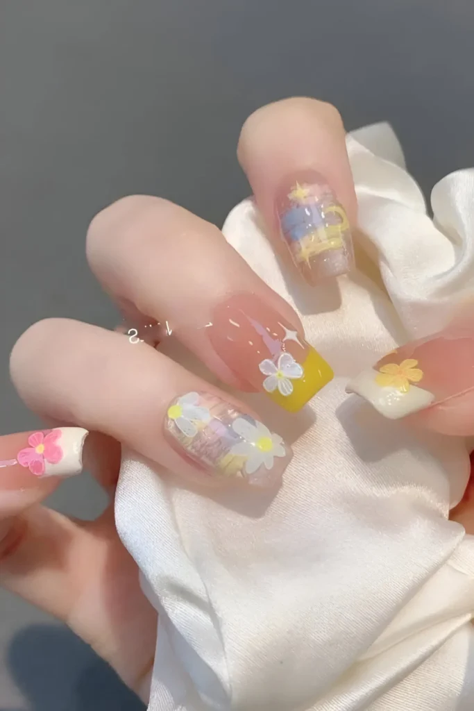 Cute nail design on medium square nails featuring pastel woven/plaid texture (yellow, blue, pink), yellow French tip, and white/pink floral decals on a sheer base.