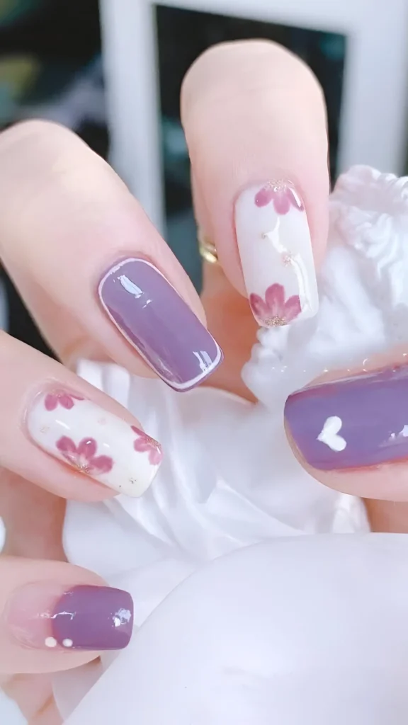 Cute nail design set in dusty mauve and white, featuring floral patterns with glitter accent, white outline on solid mauve, tiny heart motif, and mauve tip with dots on square nails.