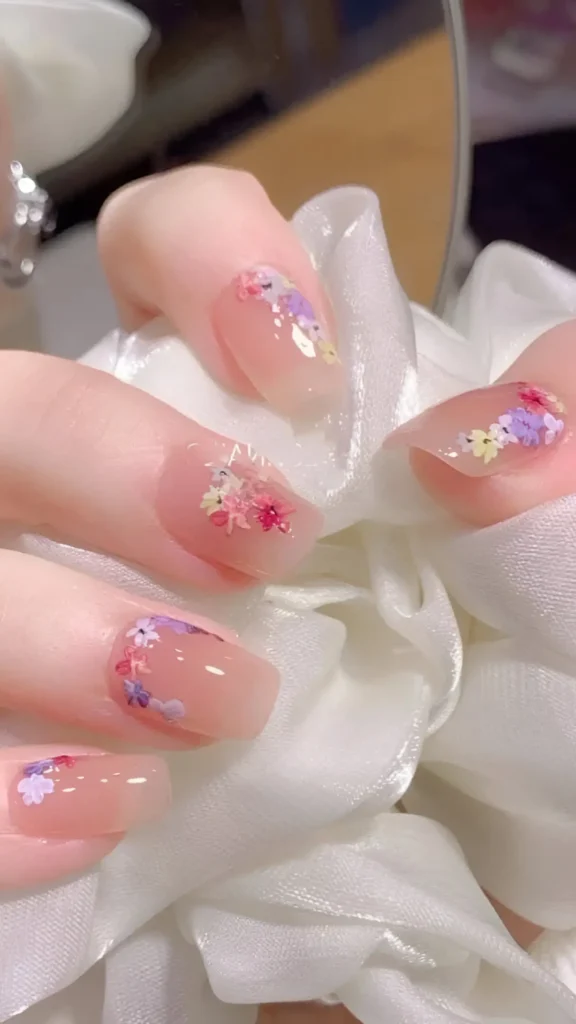 Cute nail design featuring delicate multi-color wildflower clusters (lilac, pink, yellow) placed near the tips on a sheer glossy base; medium almond-shaped nails.