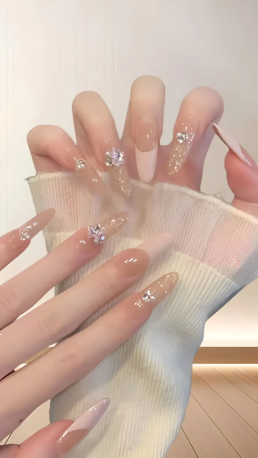 Cute long almond nails with sheer nude base, subtle glitter, and clear crystal 3D bow charms.