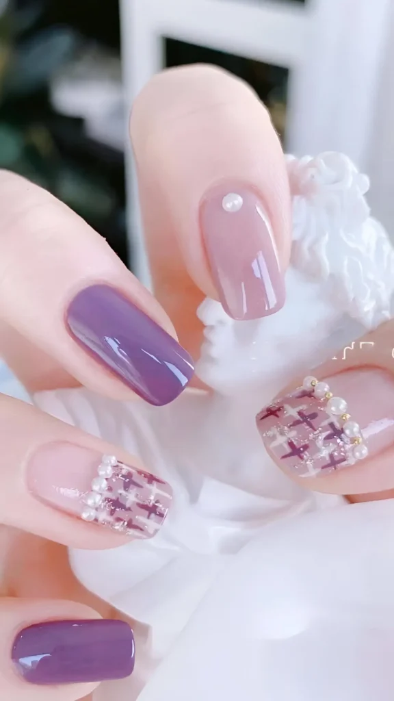 Cute nail design featuring solid purple gloss and sheer pink nails with pearl accents, plus accent nails with purple/white tweed/plaid pattern tips lined with pearls; medium square shape.