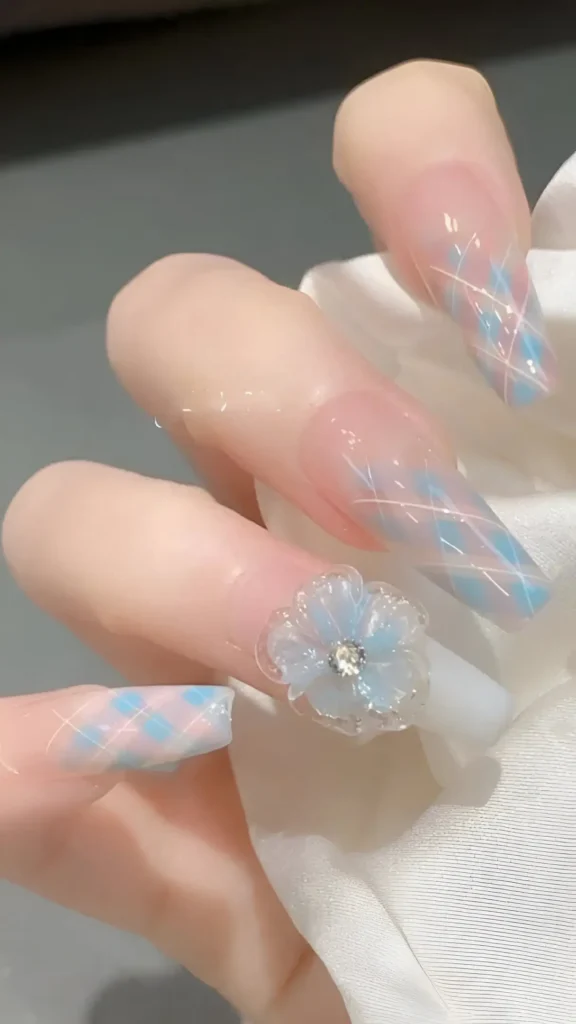 Cute nail design on long coffin nails with sheer base featuring blue and white lattice pattern tips, plus accent nail with large 3D translucent blue flower and rhinestone center.