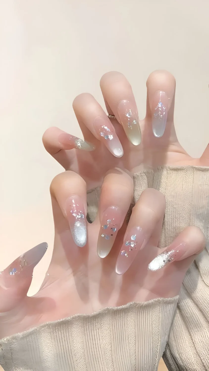 Cute long almond nails with sheer base and scattered iridescent flakes creating a fairy dust effect.