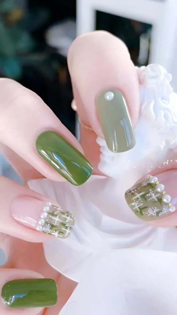 Cute nail design featuring solid olive green and sheer pink nails with pearl accents, plus accent nails with green/cream tweed/plaid pattern tips lined with pearls; medium square shape.