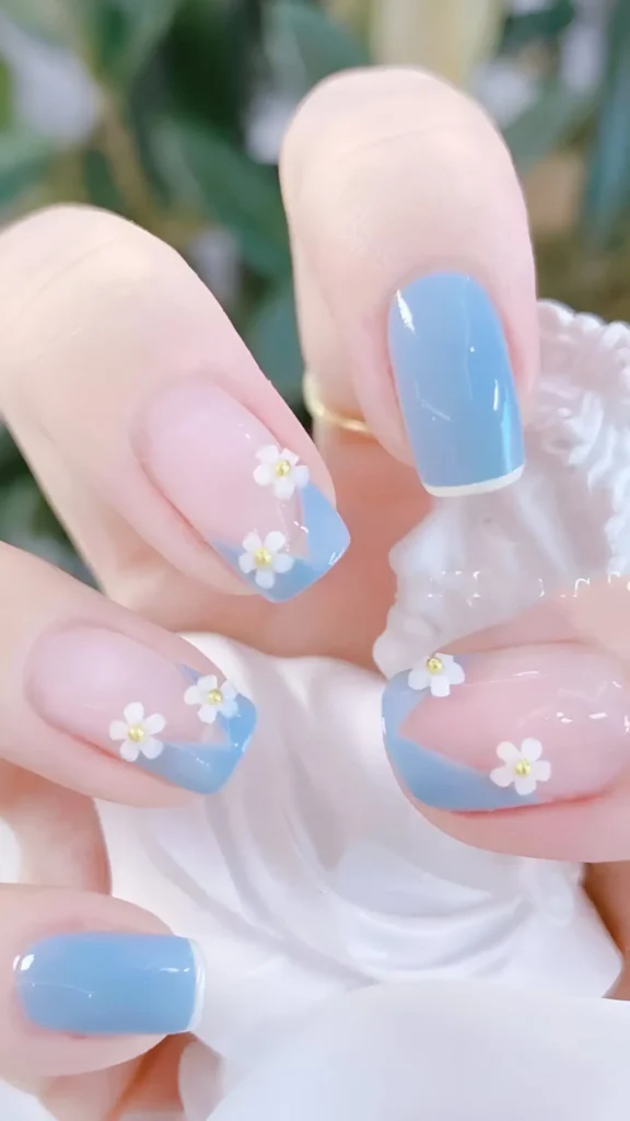 Cute nail design featuring wavy sky blue French tips on a sheer base, adorned with small white daisy flowers with gold centers; includes solid sky blue accent nails on square shape.