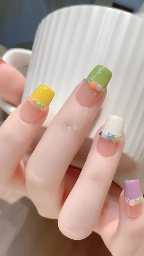 Cute nail design with sheer base and color block French tips (yellow, green, white, purple) accented by a line of tiny multi-color beads; square shape.