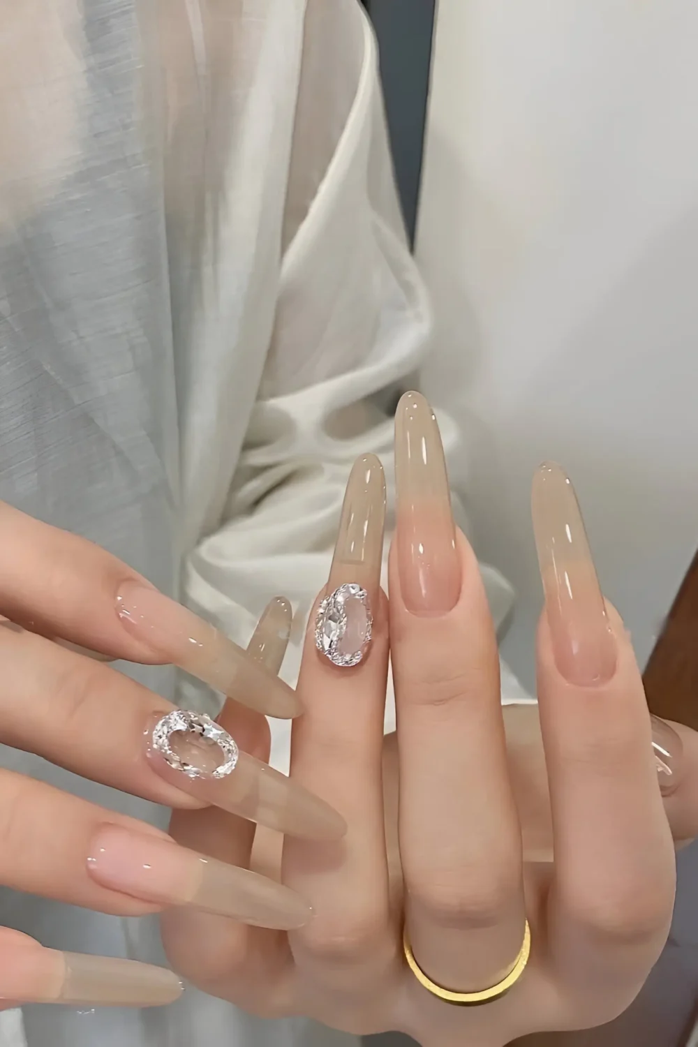 Cute long stiletto nails with sheer nude base and large statement clear crystal gem accents.