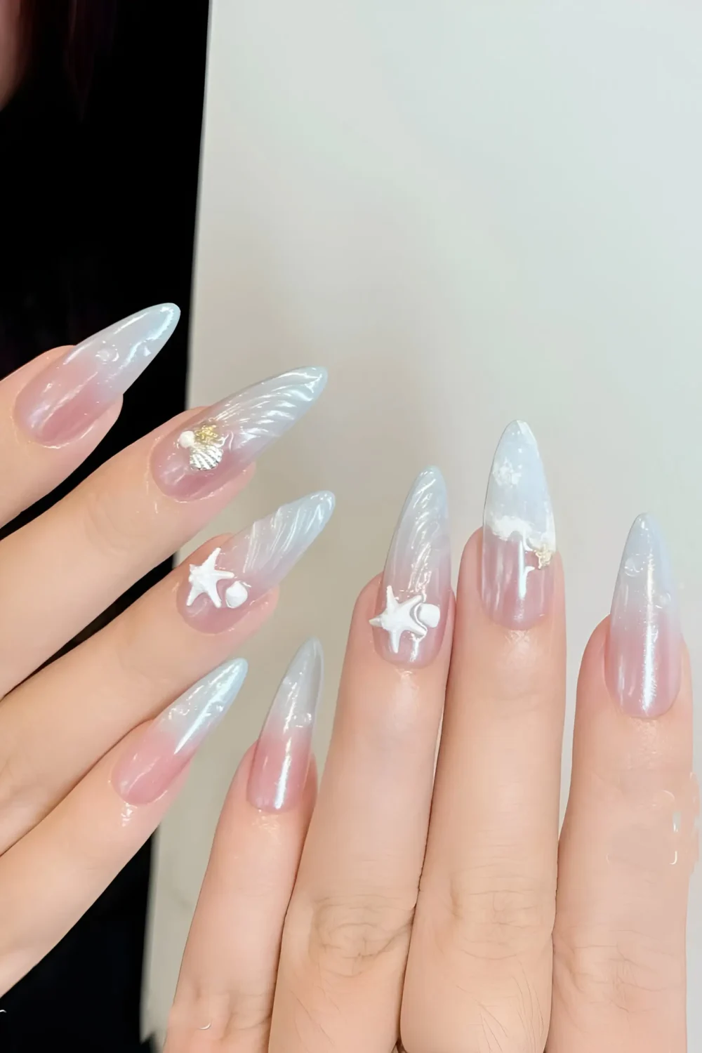 Cute long stiletto nails with sheer base, iridescent pearly tips, and 3D seashell and starfish charms.