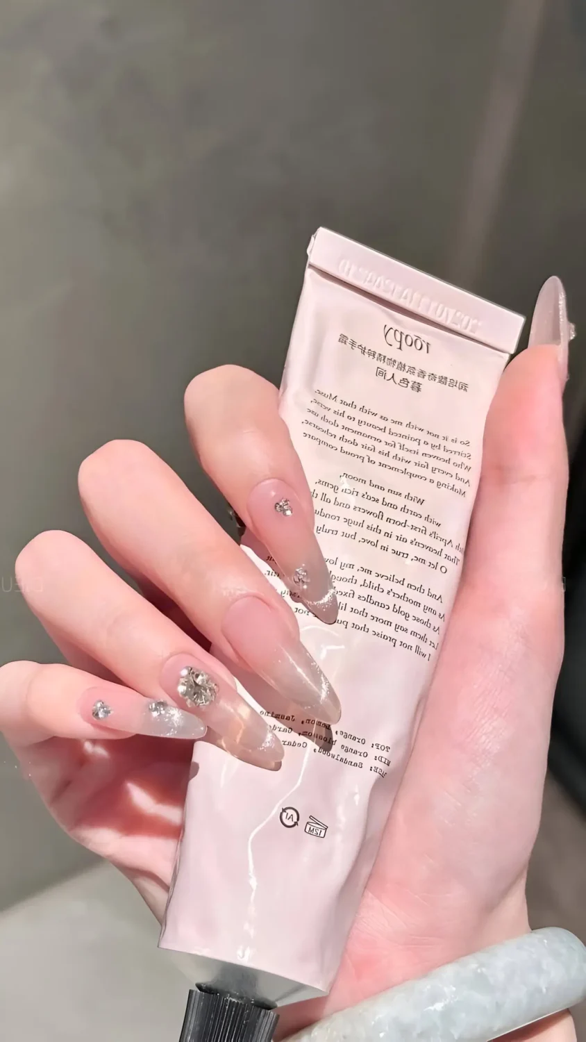 Cute long almond/stiletto nails with sheer base, silver shimmer or cat-eye effect, and clear crystal cluster accents.