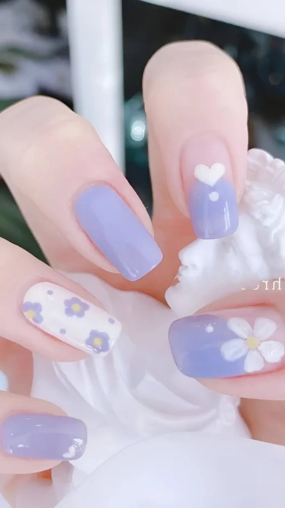 Cute nail design featuring lavender nails with white heart or large white flower accents, plus white nails with scattered lavender flowers; square shape.