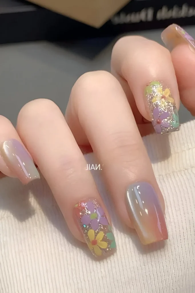 Cute nail design mixing iridescent shifting colors (pink, lilac, green) with silver glitter nails overlaid with simple yellow flowers; square shape.