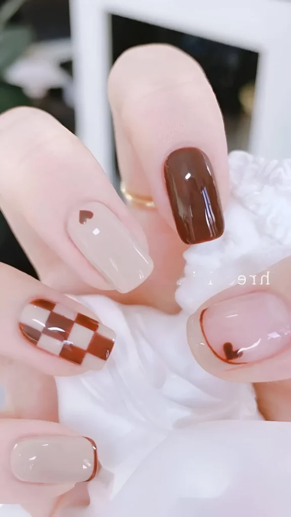 Cute nail design mixing chocolate brown and beige; includes checkerboard pattern, heart accents (solid and outlined), micro French tip, and solid brown nail; square shape.