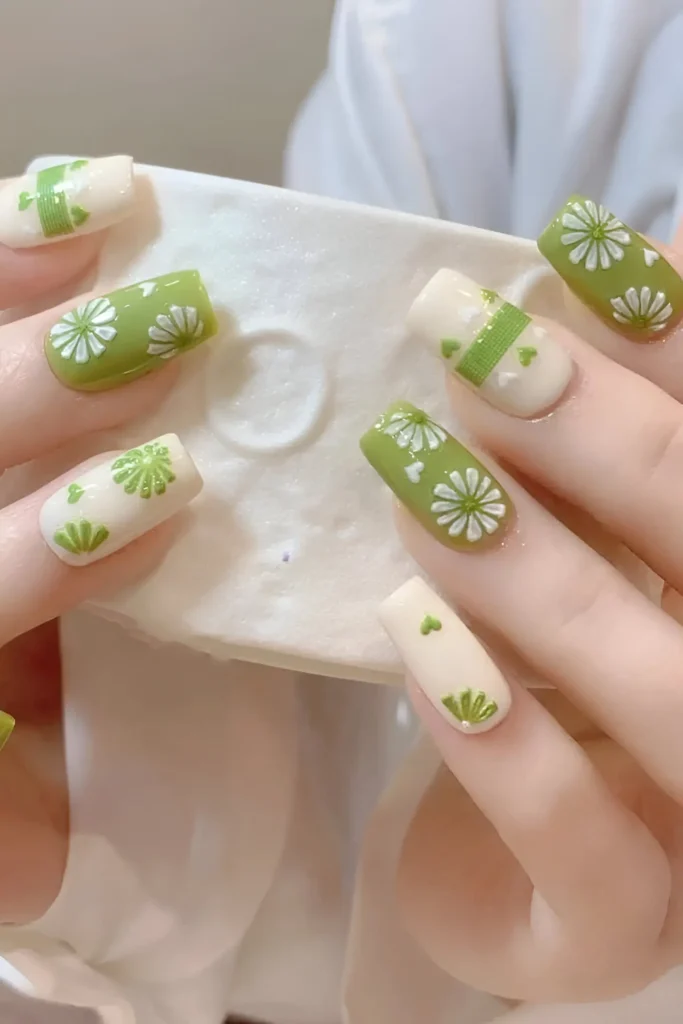 Cute nail design mixing olive green base with white graphic floral/starburst patterns, and white base with green heart/band motifs; square shape.