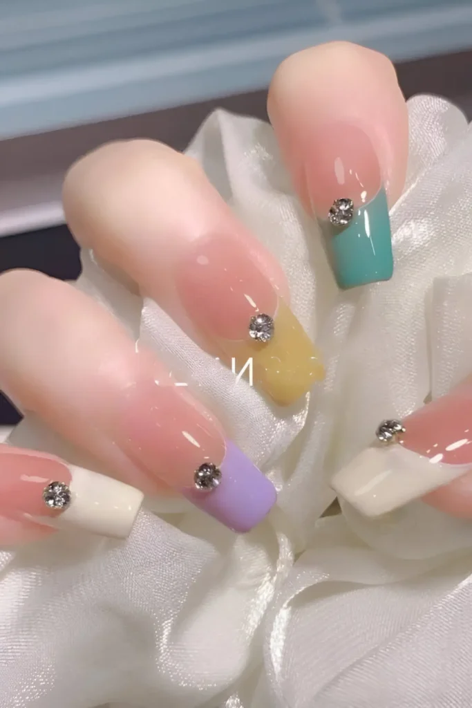 Cute nail design on long square nails with sheer base and solid color block French tips (teal, yellow, lavender, white), each accented with a single rhinestone at the smile line.