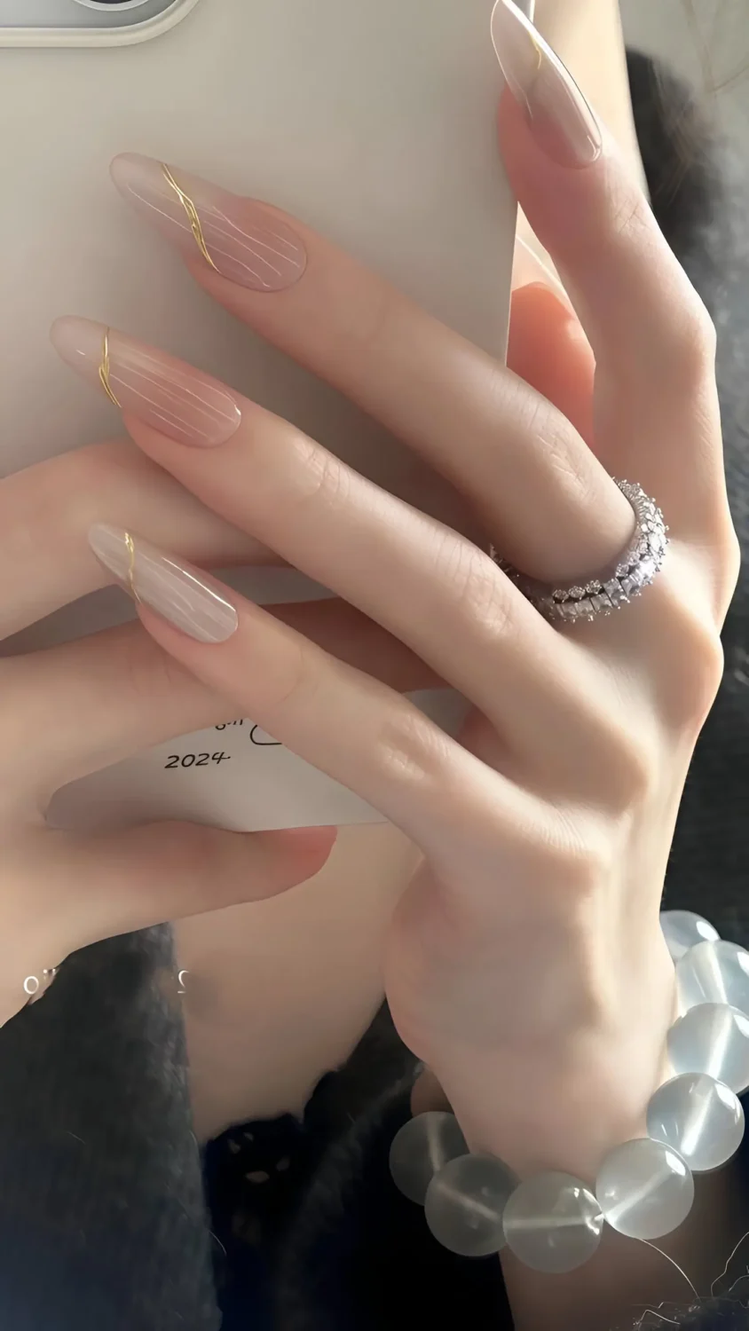 Cute long stiletto nails with sheer textured base and delicate curved gold metallic line accents near cuticles.