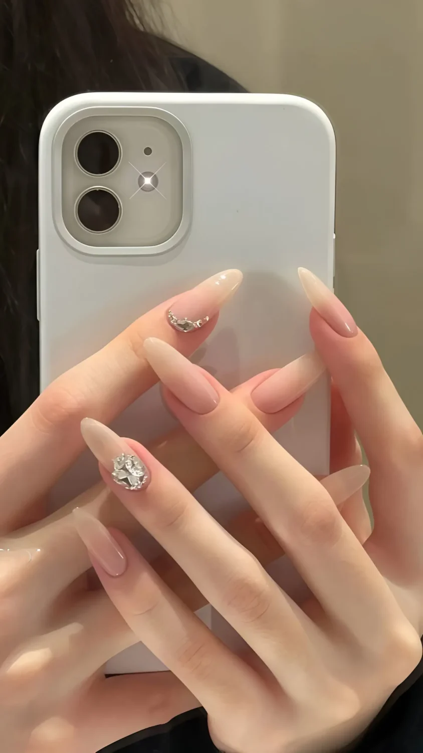 Cute long almond nails with solid opaque nude base and intricate clear crystal cluster accents near cuticle.