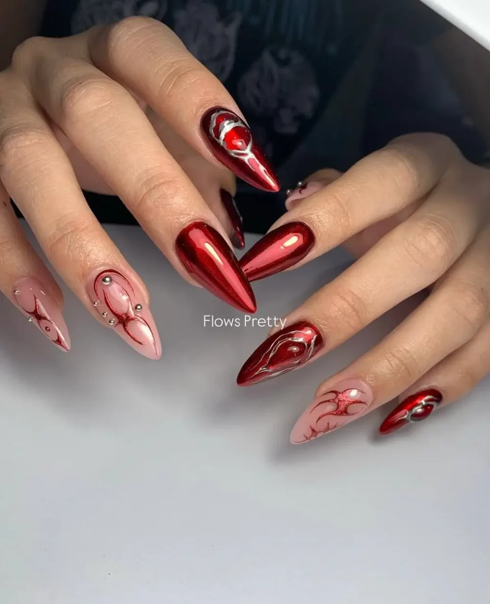 Sharp stiletto nails with fiery metallic red chrome, abstract tribal-style designs in red and silver chrome, and 3D silver sculptural accents.