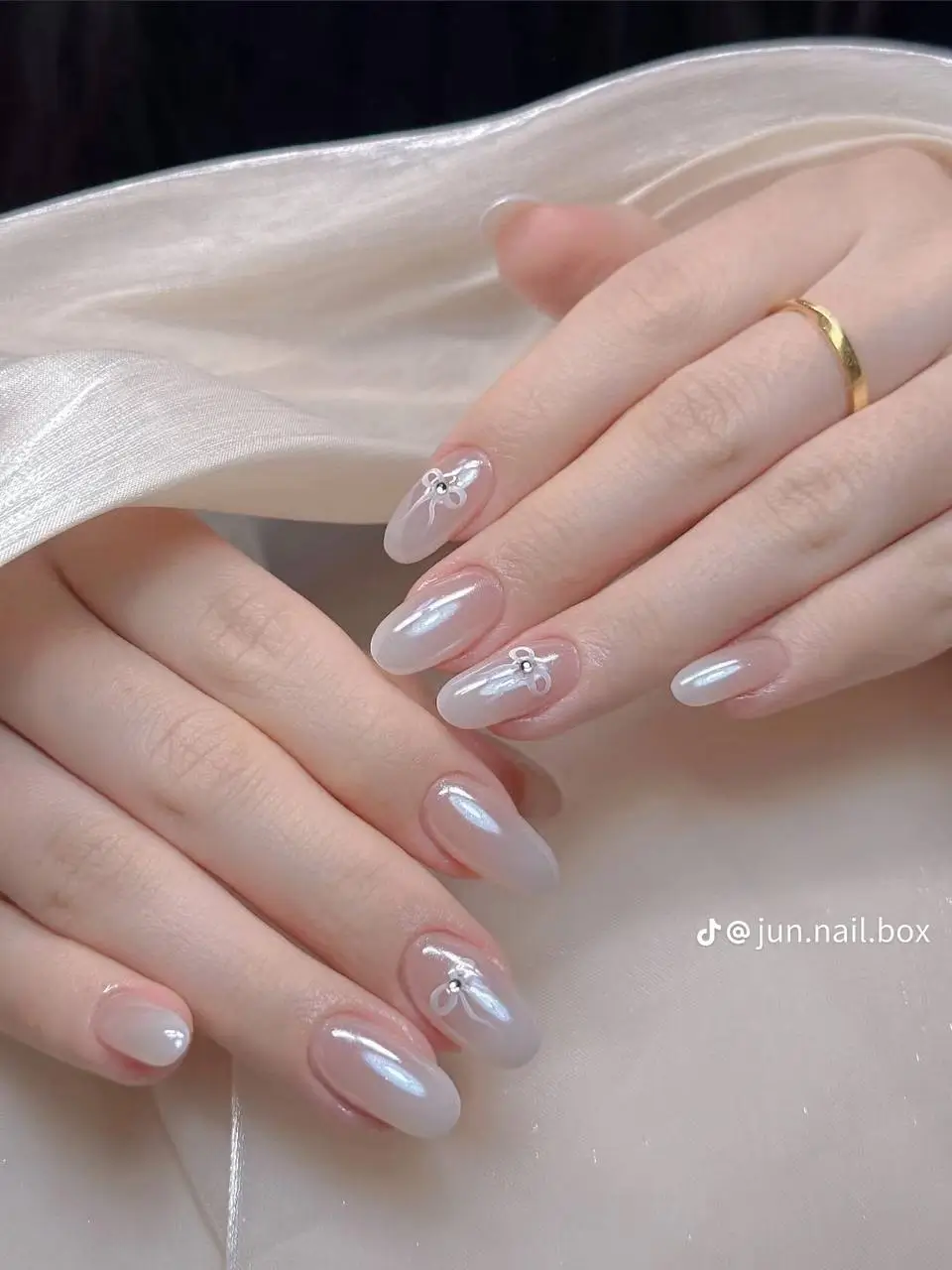 Delicate almond-shaped nails with a sheer pearlescent milky white finish, accented with dainty 3D white bow embellishments; a popular nail style for 2025.