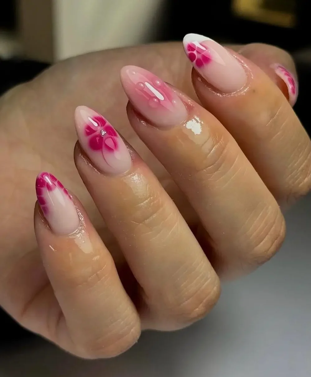 Almond nails displaying an ethereal magenta watercolor flower design on a sheer base, with soft white tips and rhinestone centers.
