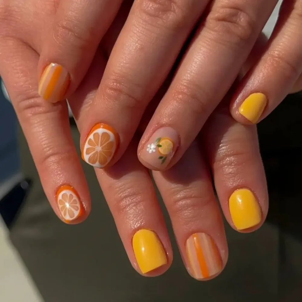 Cheerful orange-themed nail art with citrus slices, stripes, and a floral accent on short nails.