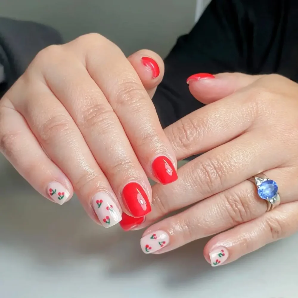 A classic red manicure with accent nails featuring tiny cherry heart designs.