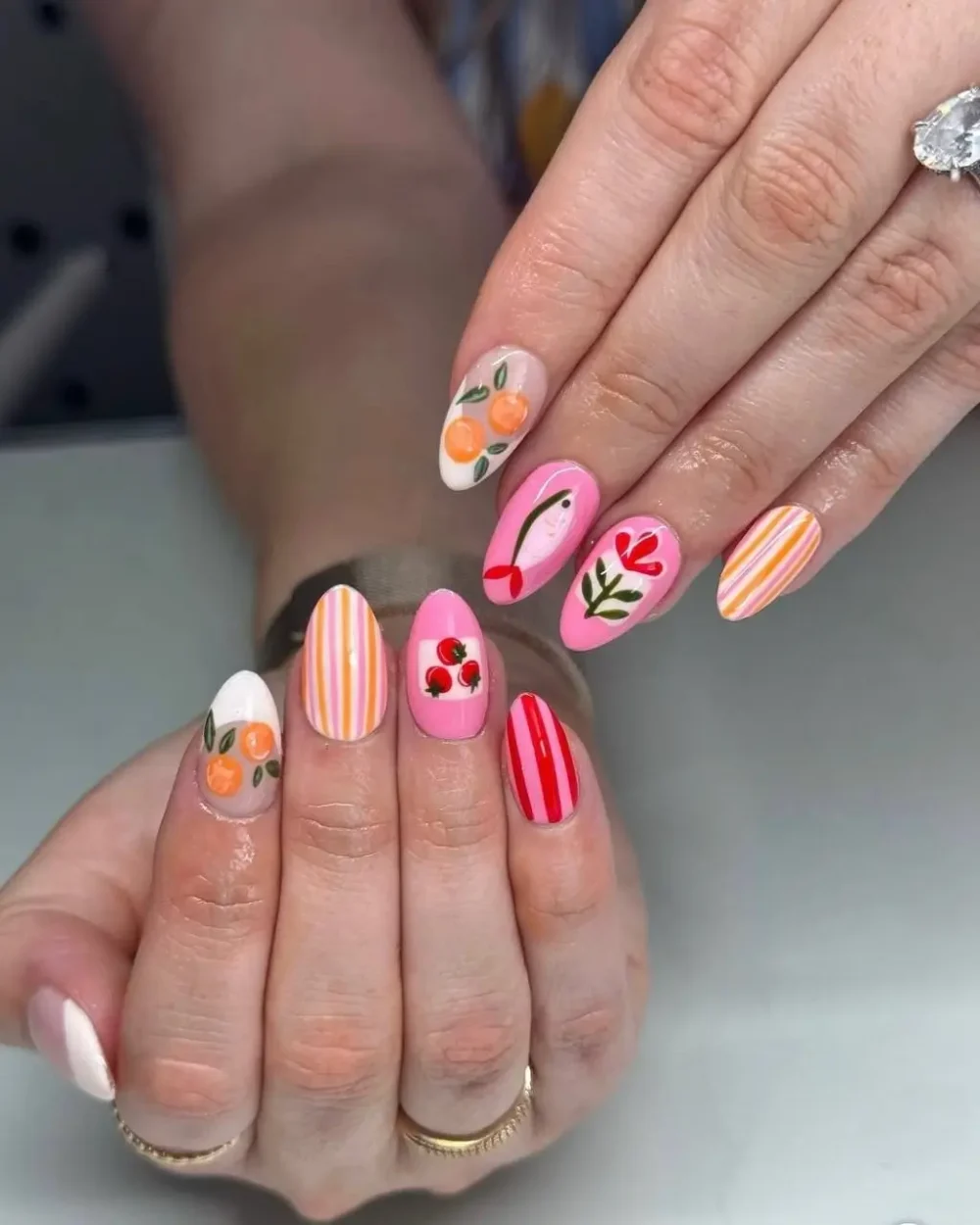 An eclectic, mismatched manicure with pink and orange fruit, floral, and striped nail art.
