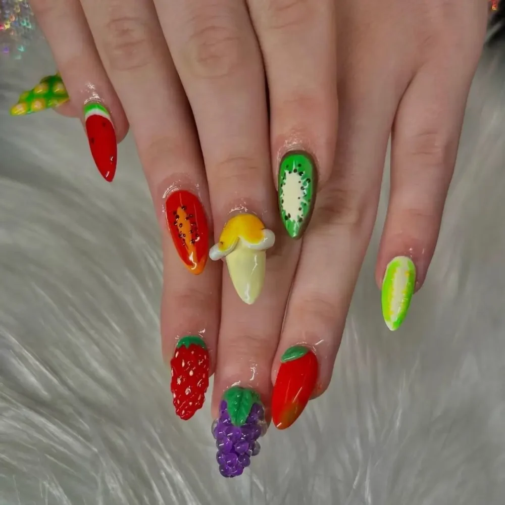 Highly detailed 3D fruit nail art including grapes, strawberries, and kiwis on long nails.