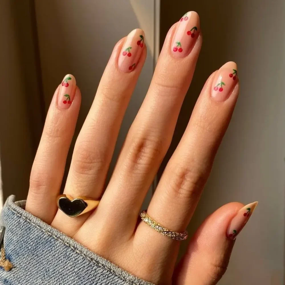 A minimalist manicure with a scattered pattern of tiny cherries on sheer, almond-shaped nails.