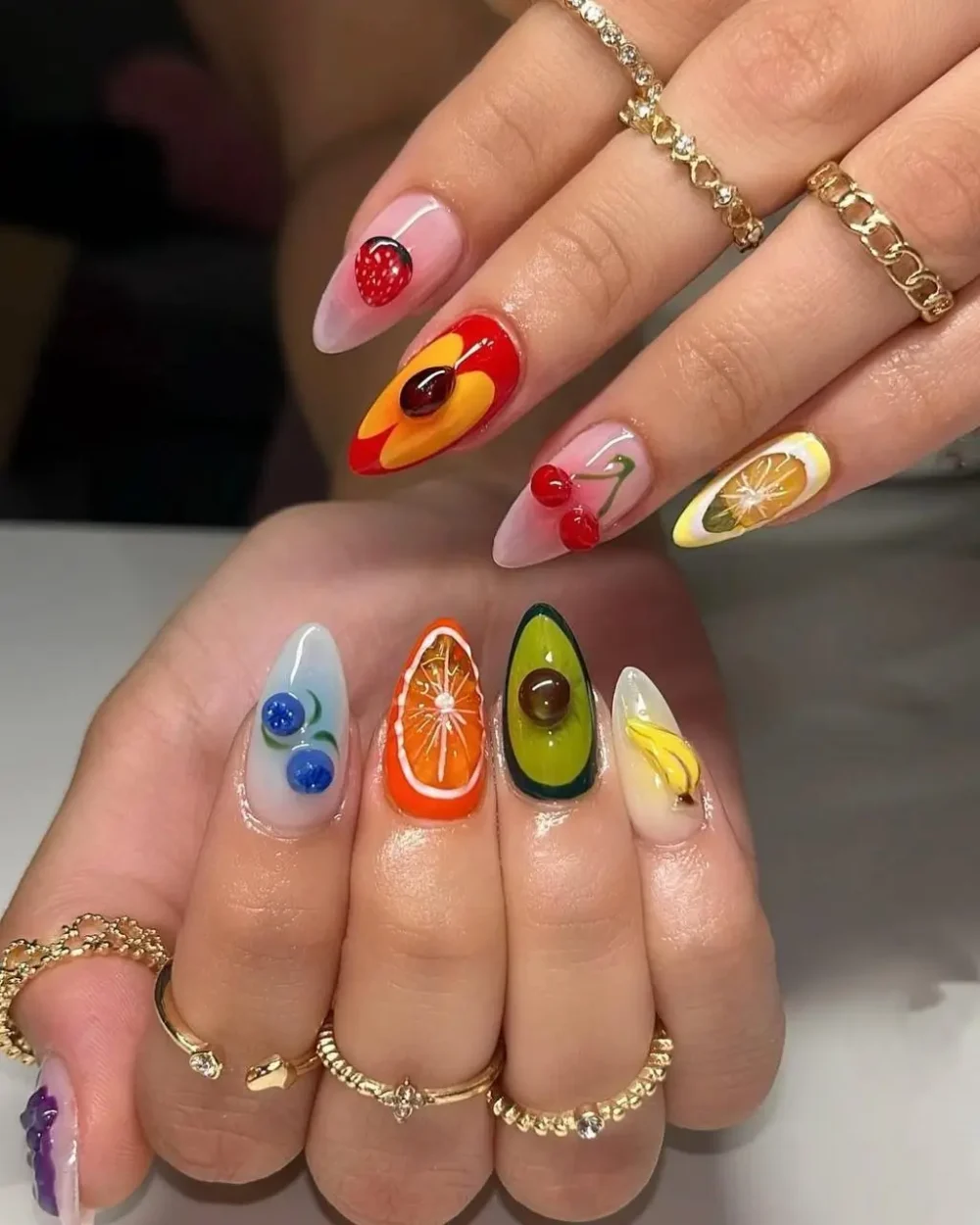 A close-up of a dimensional fruit medley manicure, including 3D avocado, peach, and orange slices.