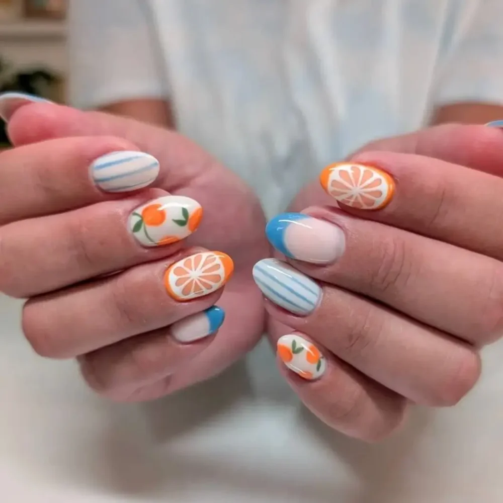 A mixed-pattern manicure with orange fruit nail art, blue stripes, and blue French tips.