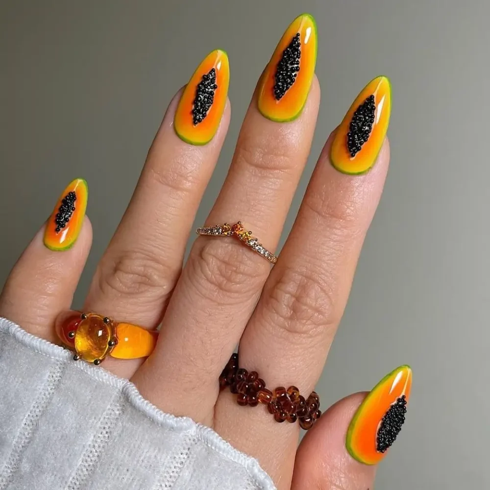 A close-up of long nails with a vibrant papaya fruit design and textured black seeds.