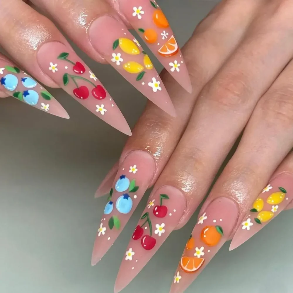 Detailed, illustrative fruit and flower art on long, stiletto-shaped nails with a nude base.